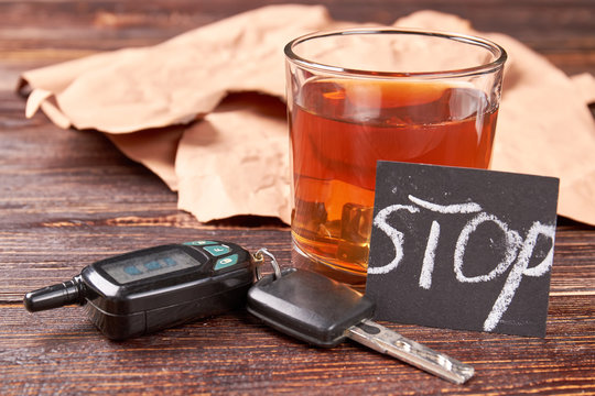 Alcohol beverage, car keys, note. Brown alcohol beverage in glass, car keys, message stop on wooden background. How to stop alcohol drinking concept.