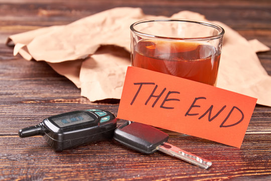 Message the end, alcohol, keys. Glass of alcohol, car keys, note the end on wooden background. Drinking and driving leads to death.