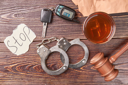 Glass of whiskey beside handcuffs. Alcohol drink, gavel, handcuffs, car key, message stop, top view. Booze driving concept.