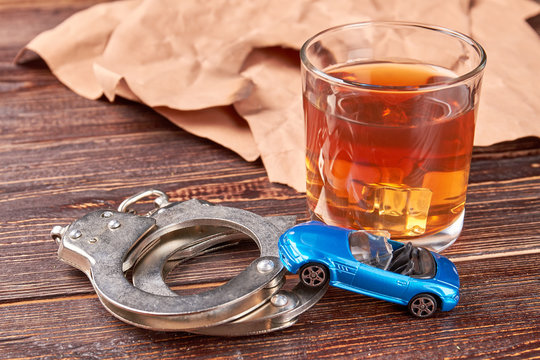 Metal handcuffs, car, whiskey glass. Drink and driving concept.