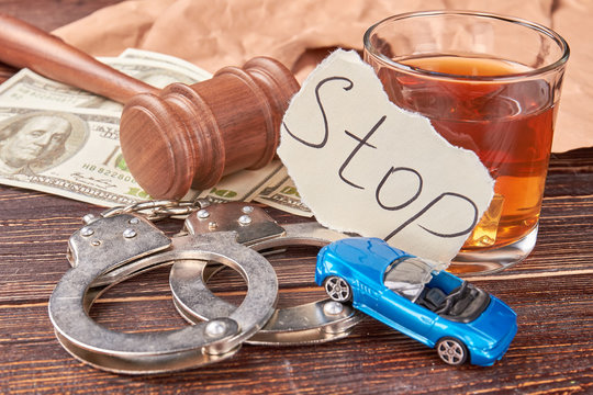 Still life drunk driving. Handcuffs, car, whiskey, american money, gavel on wooden background close up.