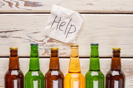 Help to be saved from alcoholism. Paper message above set of bottles with alcohol.