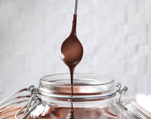 Jar with delicious chocolate sauce and spoon on light background