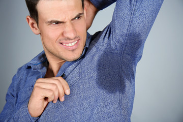 Handsome young man with wet spot on clothes under armpit against grey background. Concept of using...