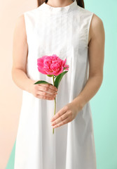 Young woman holding beautiful peony flower on color background