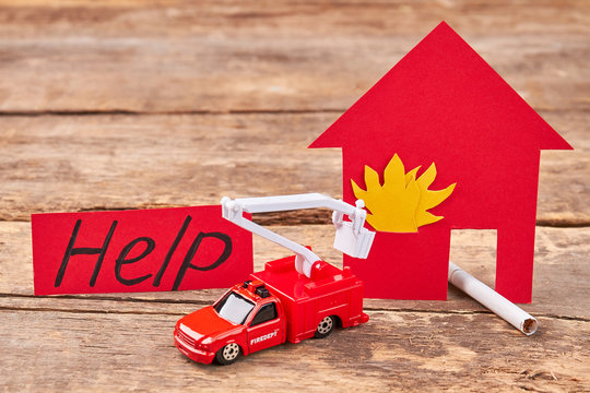 Flaming house, cigarette, toy fire truck. Message help, toy lorry, flame, wooden background.
