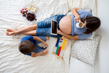 Young pregnant woman and her child, lying in bed with tablet