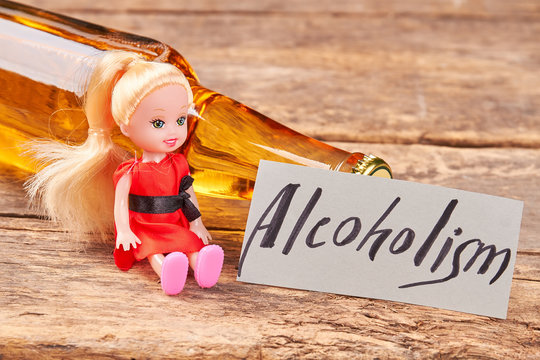 Lying bottle, doll, paper message. Full bottle of beer, toy, text alcoholism, wooden background.