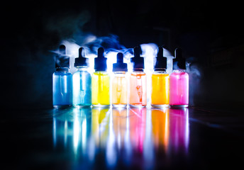 Vape concept. Smoke clouds and vape liquid bottles on dark background. Light effects. Useful as background or vape advertisement or vape background. Selective focus