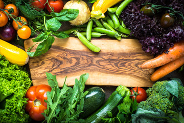 Frame of fresh vegetables around cutting board.