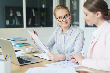 Young businesswoman pointing at document while talking to co-worker