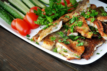 Fried fish with fresh tomatoes, cucumbers and parsley on a white dish. Close up.