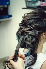 Naklejka premium Closeup of a professional hairdresser's hands doing a hairstyle in a beauty salon. Model of a brunette with long hair. The concept of fashionable stylish hairstyle, professional work with hair.