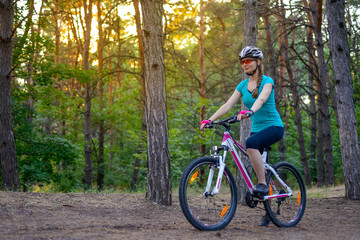 Fototapeta na wymiar Young Woman Riding the Bike on the Trail in Beautiful Fairy Pine Forest. Adventure and Travel Concept.
