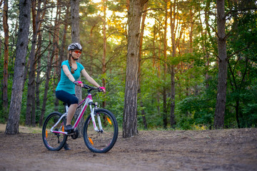 Fototapeta premium Young Woman Riding the Bike on the Trail in Beautiful Fairy Pine Forest. Adventure and Travel Concept.