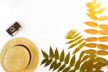 Straw hat with green leaves and old camera on white background, Summer background. Top view. Sun flare