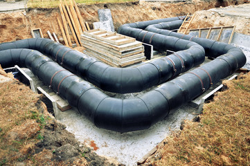 The process of laying of engineering heating systems. Two turning black plastic pipes in sandy...