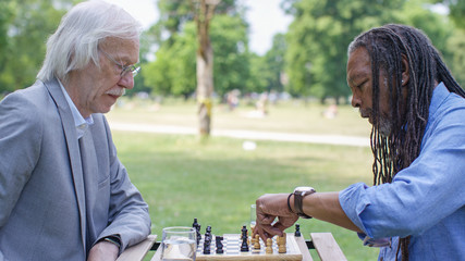 Two senior men playing a game of chess outdoors in the park - 164465990