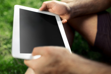 Young man using and typing tablet computer in summer grass.