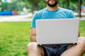 Young man using and typing laptop computer in summer grass.