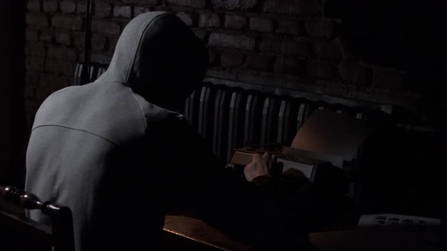 Young hooded male writer with typewriter. Hipster hooded man using a typewriter at work