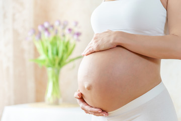 belly of caucasian pregnant woman in light room with flowers