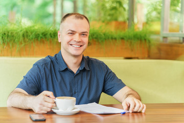 adult man is sitting at cafe and smile working with phone and paper