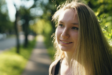 teen girl smiling in green town in sunny summer evening