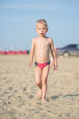 Baby boy walking on the sandy beach near the sea. Cute little kid at sand tropical beach. Ocean coast.