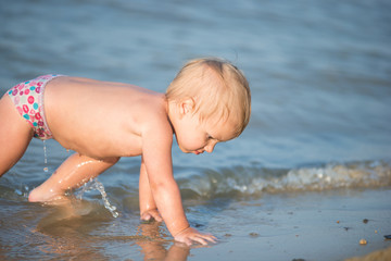 Fototapeta na wymiar Baby playing on the sandy beach and in sea water. Cute little kid with toys on sand tropical beach. Ocean coast.