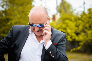 Mature stylish man in classic costume and sunglasses talk to telephone