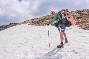 a boy on the snow on a trek with a bag and trekking poles going up at the Carpathian mountains in summer