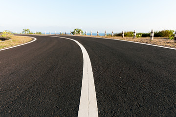 New Asphalt coastal road with white markings going round cliff edge bend, with blue sea and clear sky back drop.