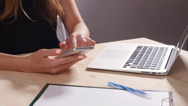 A girl is working in the office behind a computer with a smartphone
