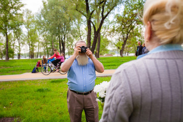 elderly man with a beard is making a photo of a wife with flower