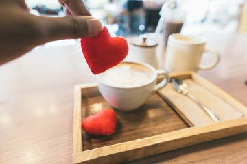 Hands holding a small heart to be put into the coffee in selective focus. Concept : art, love coffee, attention