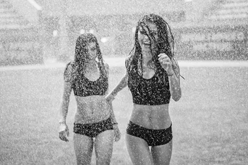 Fotobehang Two charming cheerleaders having fun with irrigation on a football field (black and white) © flywish