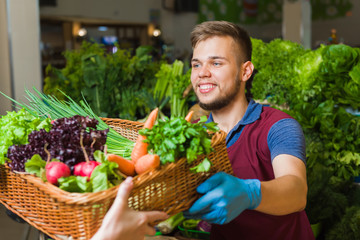 A friendly male seller posing with a huge basket of vegetables. Fresh vegetables in the background.