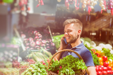 A man with a basket at farm market. The man is talking on the phone.