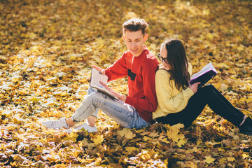 Series photo of beautiful young brunette woman in sunglasses and young man in red shirt sitting back to back on a fallen autumn leaves in a park and reading a book