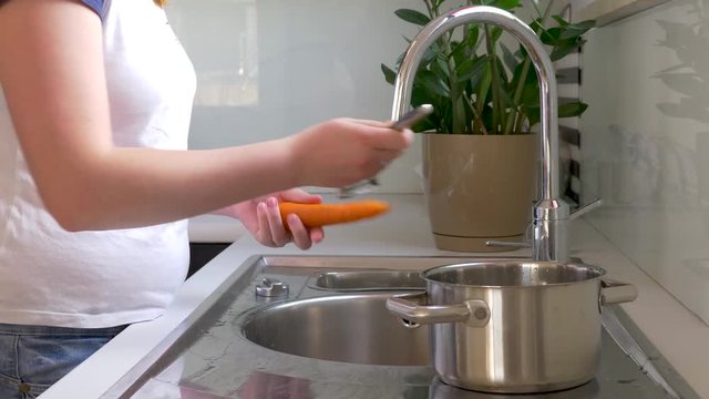 Woman peels vegetables with vegetable peeler. A woman is peeling carrots and potatoes with a vegetable peeler