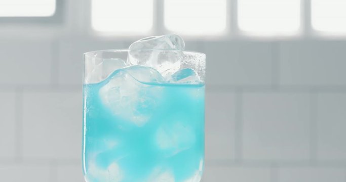 bright blue cocktail in rolling glass with ice cubes