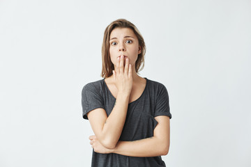 Young beautiful girl ashamed covering mouth with hand looking at camera over white background.