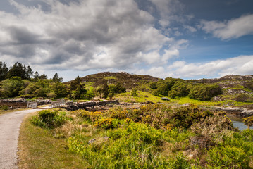 Assynt Peninsula, Scotland - June 7, 2012: Short stone bridge over creek landing into Atlantic Ocean inlet South of Loch An Arbhair under heavy sky. Forested hills and ocean waters.