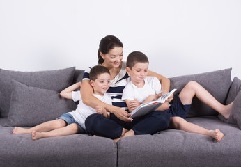 Fototapeta na wymiar Mother reads an interesting book with her sons of the sofa. Studio portrait on white background.