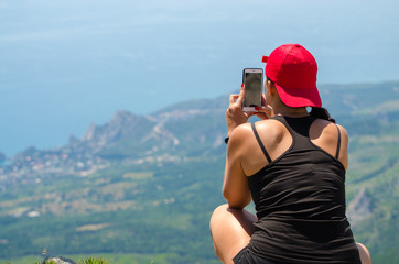 Successful sport woman backpacker treveller with baseball cap use smartphone taking photographs on seaside high mountain rock