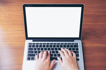 Mockup image of hand using and typing on laptop with blank white screen on wooden table in office