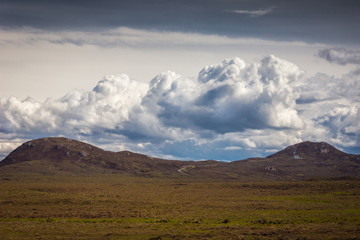 Assynt Peninsula, Scotland - June 7, 2012: Hilly scenery under gray sky with white towering clouds, dry desert-like vegetation on plateau in front, at Brae of Achnahaird. Total desolation.
