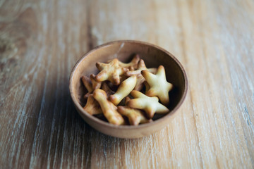 Small biscuits in many shapes in wooden cup on wood table background