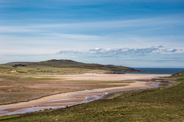 Assynt Peninsula, Scotland - June 7, 2012: Enard Bay and Atlantic Ocean under clear sky with a few white clouds.The Allt Loch Ra creek meanders over sand towards the sea. Poor green vegetation around.